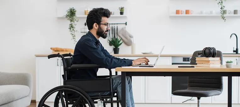 Injured employee using wheelchair while working on laptop, showing return to work support after a serious workplace injury in California.