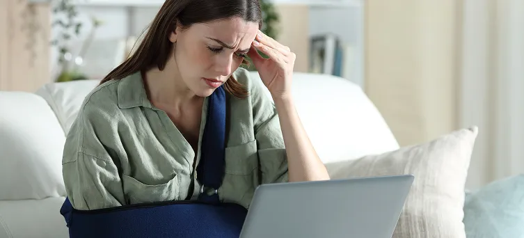 Injured worker with arm sling reviewing claim information online after denial, highlighting next steps with a workers compensation attorney in California.