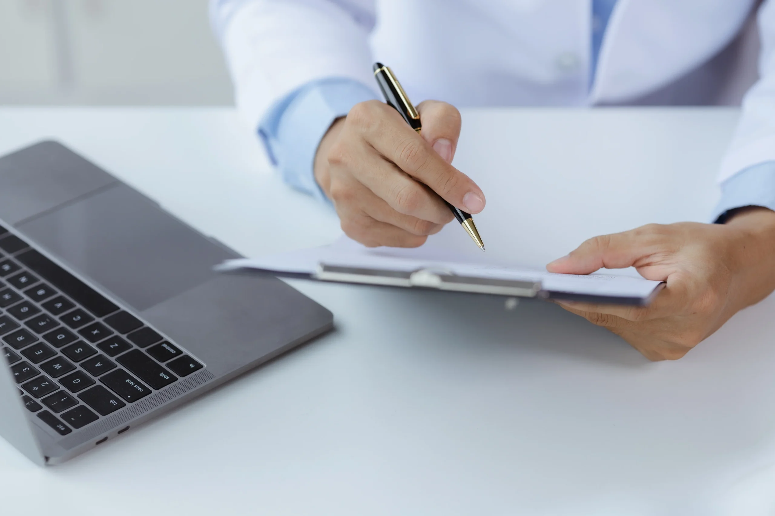 Doctor writing on clipboard beside laptop, representing treatment records and medical evidence for workers compensation cases in California.
