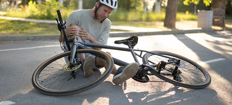 Cyclist sitting on road holding injured knee after crash representing cases handled by bicycle accident attorney Los Angeles.