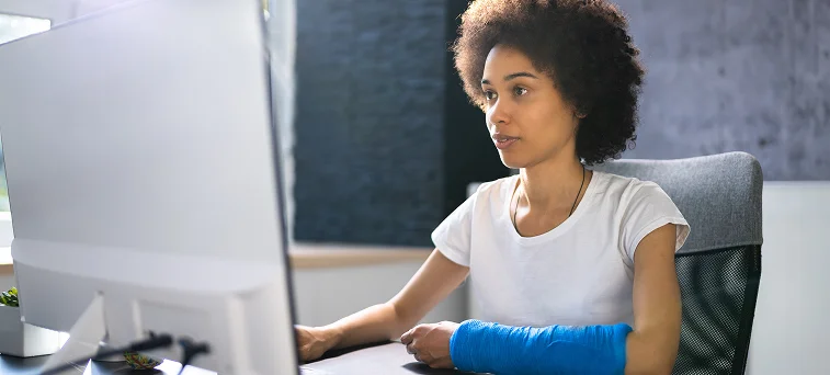 Injured employee with arm cast working at computer representing workers compensation claims handled by workers compensation attorneys in California.